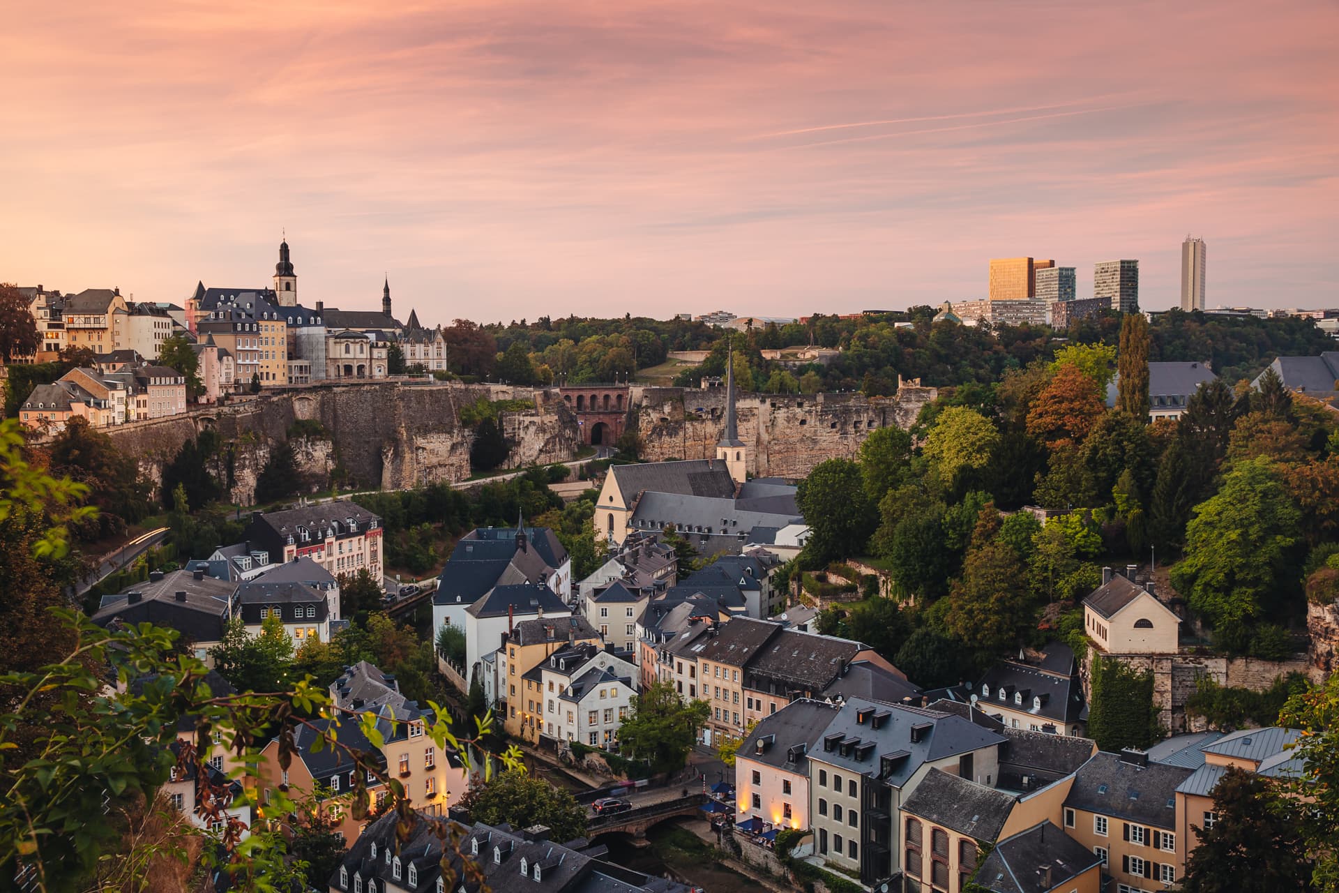 Panoramic view of Luxembourg City's Grund and old fortifications at pink dusk, Kirchberg beyond